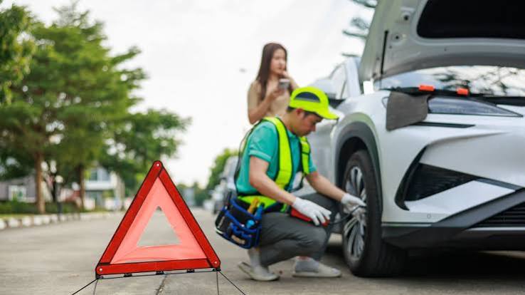 Roadside technician in a high-visibility jacket working on a car wheel on the shoulder of a road