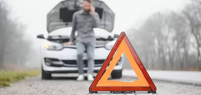 Driver on the phone beside a disabled car with a hazard triangle placed behind it